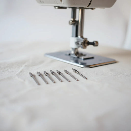 Assorted sewing machine needles and a blurred presser foot on fabric swatches for needle size matching